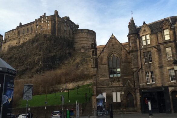 From a square, we look up at Edinburgh castle from below with stone buildings on the right