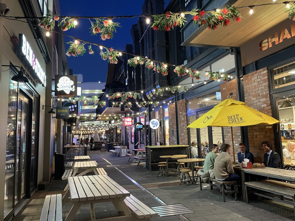 A street at night with strings of fairy lights with mistletoe hanging over the alleyway with benches on either side and restaurants