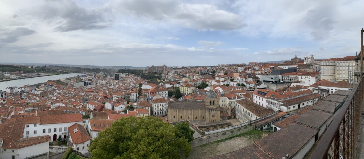 A river runs on the left with a panoramic view of the city with red tiled roofs and an old stone church on the right