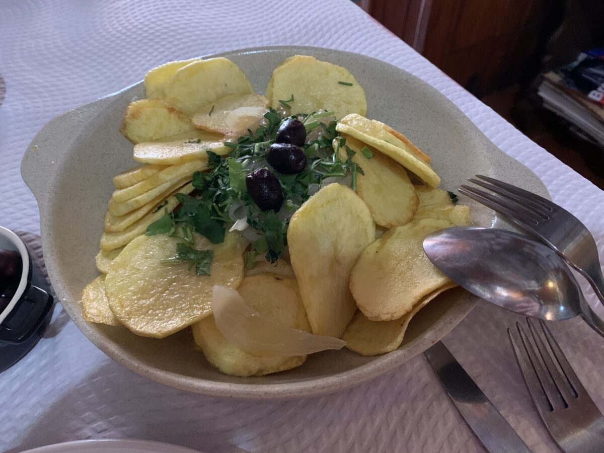 A white bowl sitting on a table with a white tablecloth filled with sliced baked potatoes with green garnish on top