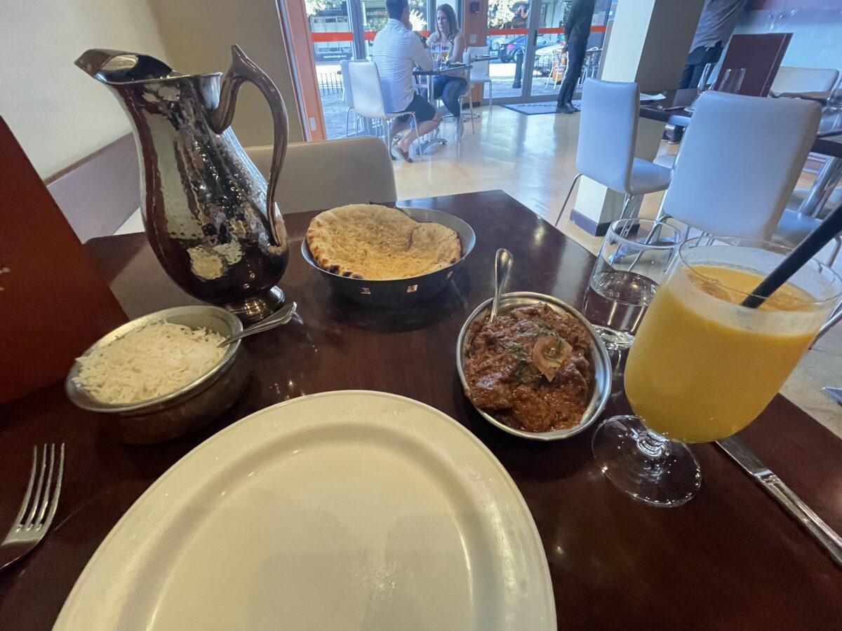 Mango lassi, indian curry, rice, and naan displayed on a wooden table