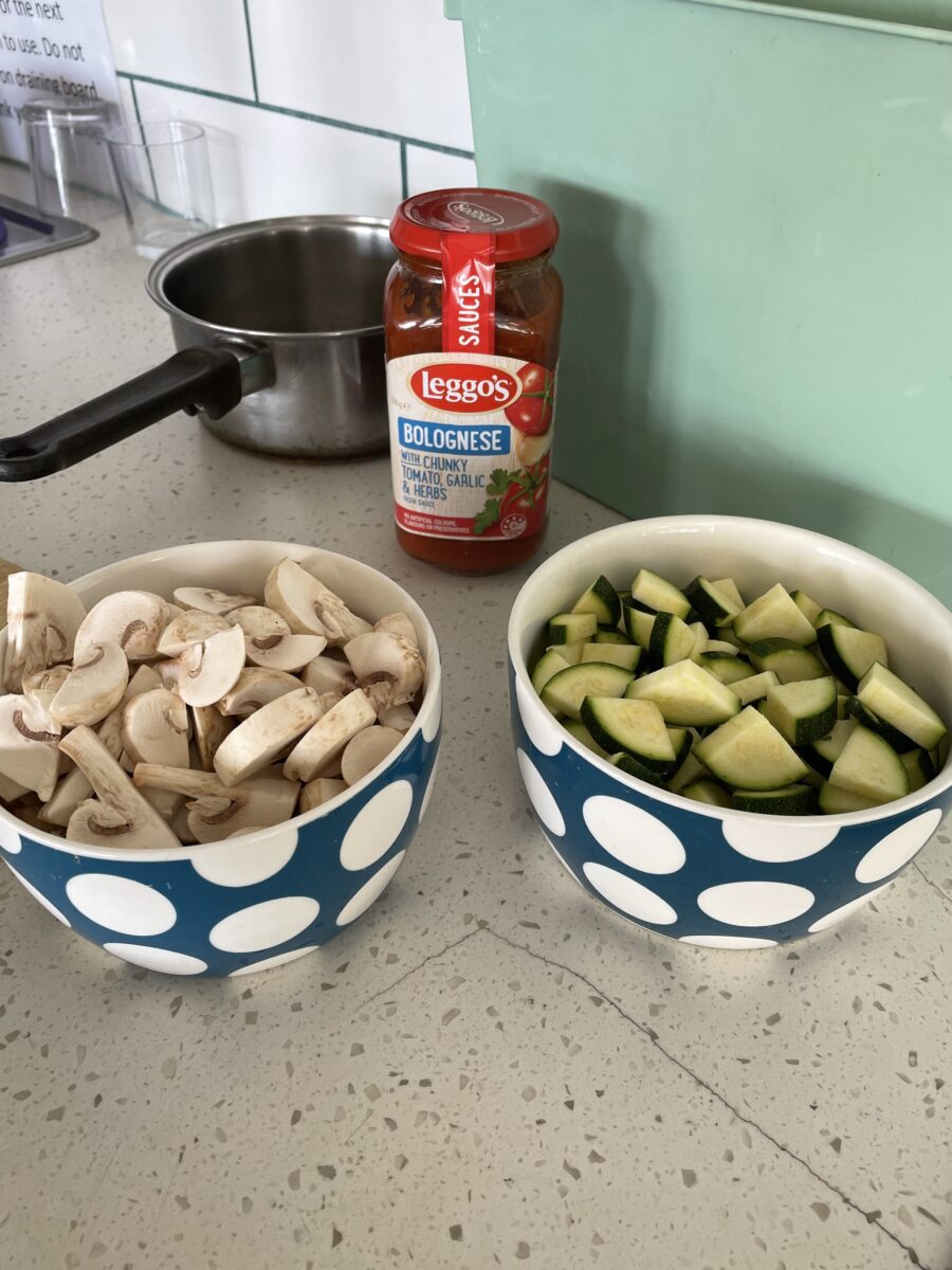 kitchen countertop with two bowls, one with cut mushrooms and the other with cut zucchini, next to a jar of pasta sauce and a pot