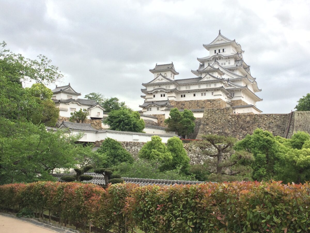 A white stone Japanese castle with many tiered roofs with lush gardens in front