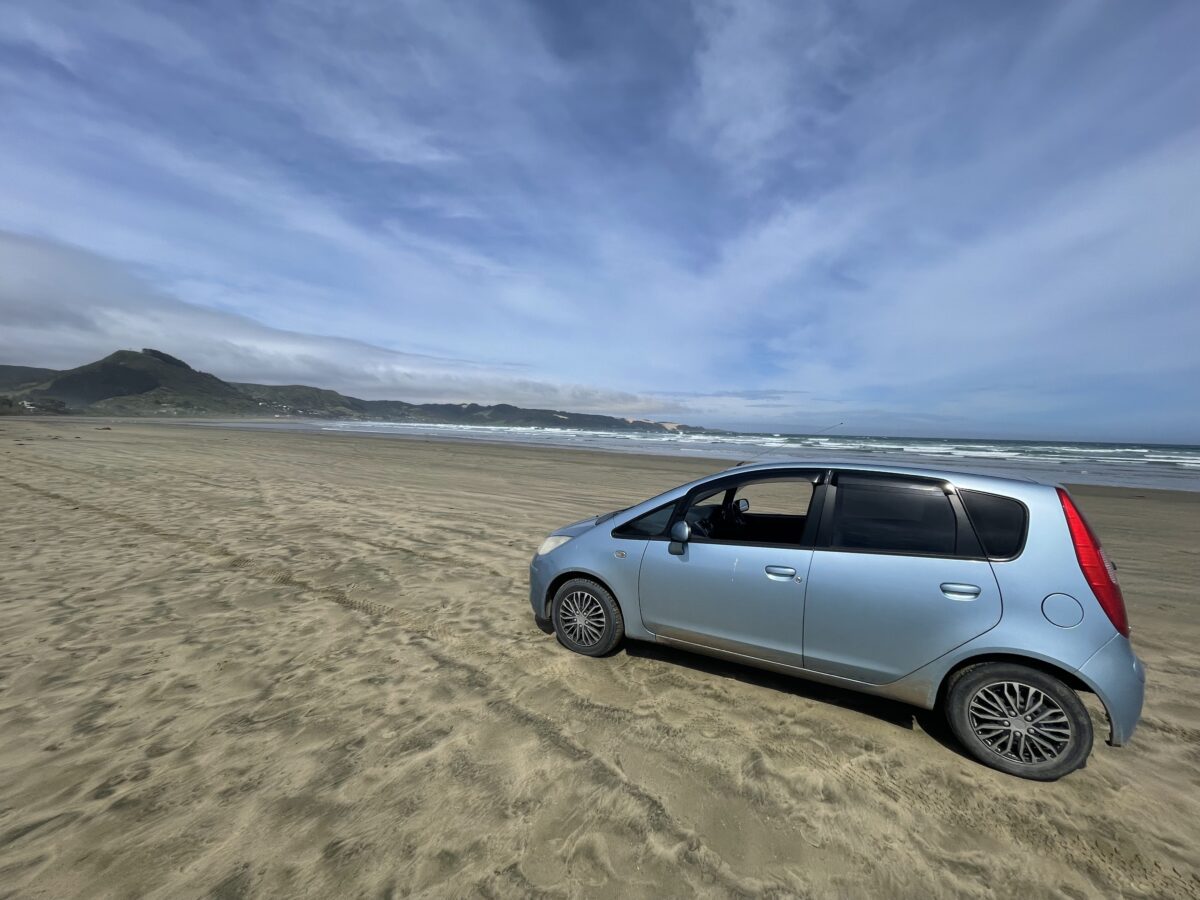 A small blue car sits on the sand at 90 Mile Beach