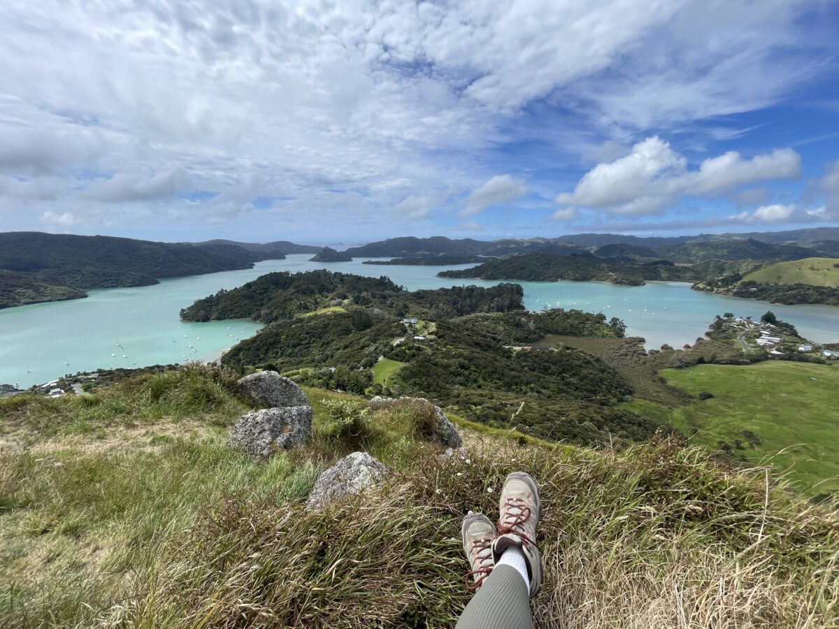 A pair of hiking boots in the foreground overlooking a blue bay scattered with green islands
