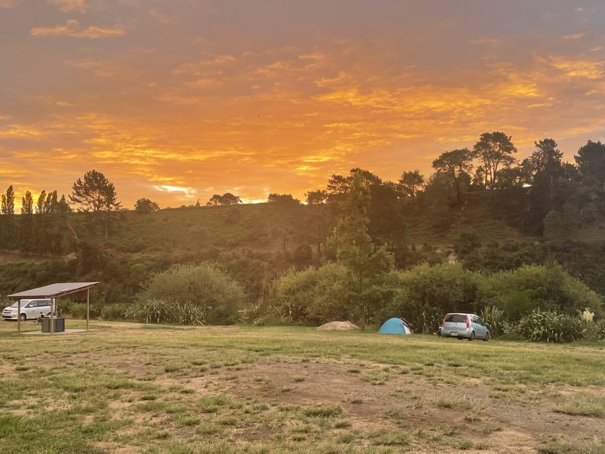 A bright orange sunset over the bush with a few camping sites set up.